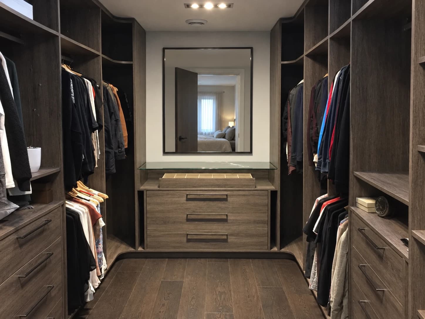 Dark U-shaped walk-in closet with a low cabinet and wall mirror.