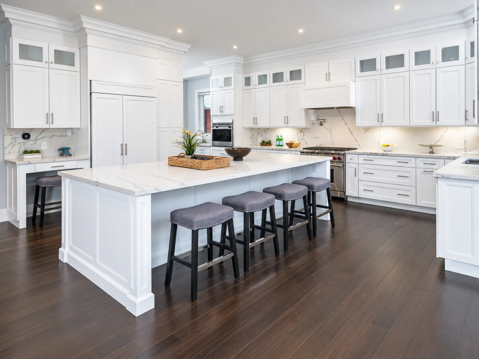 Completed transitional kitchen with white profiled cabinetry, glass transom doors, layered crown moulding and a central island with seating