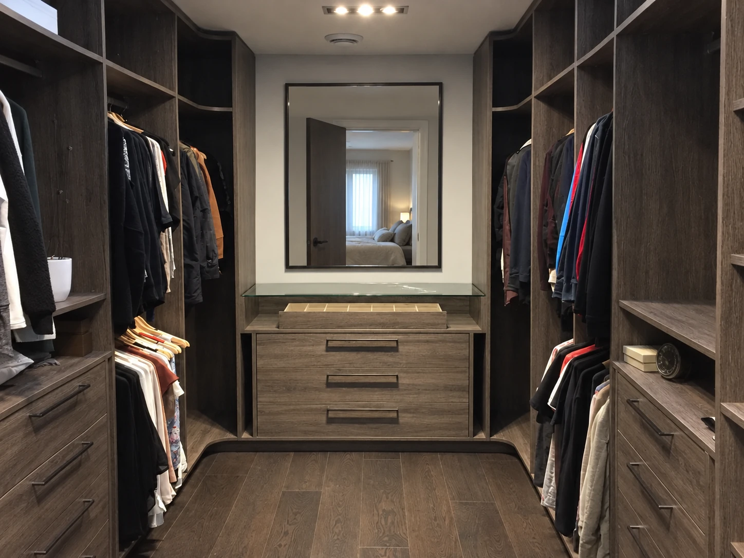 Dark U-shaped walk-in closet with a low cabinet and wall mirror.