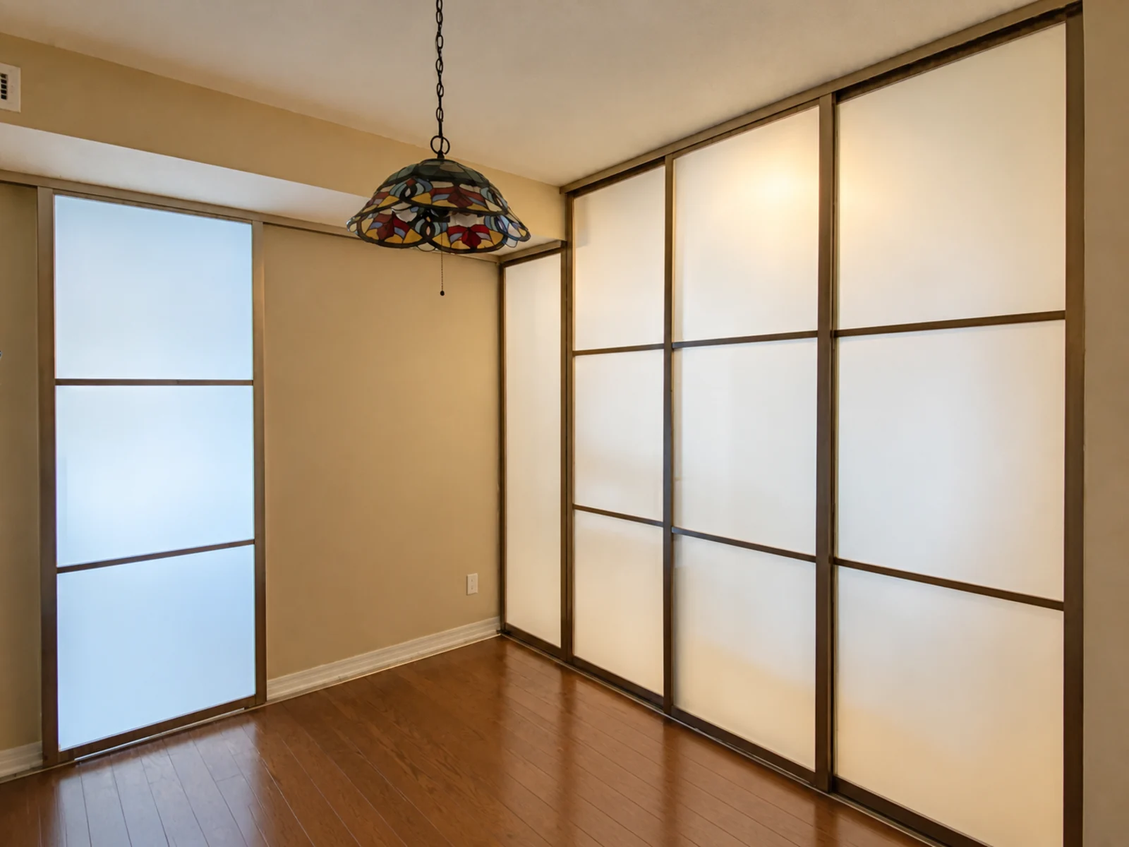 Bronze-framed frosted-glass room divider with two fixed side panels coordinated with a larger sliding run around a corner.